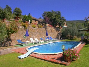 A swimming pool with lounge chairs and umbrellas, surrounded by a stone wall and greenery. - Spacious Cottage in Cortona With Swimming Pool (Cortona)