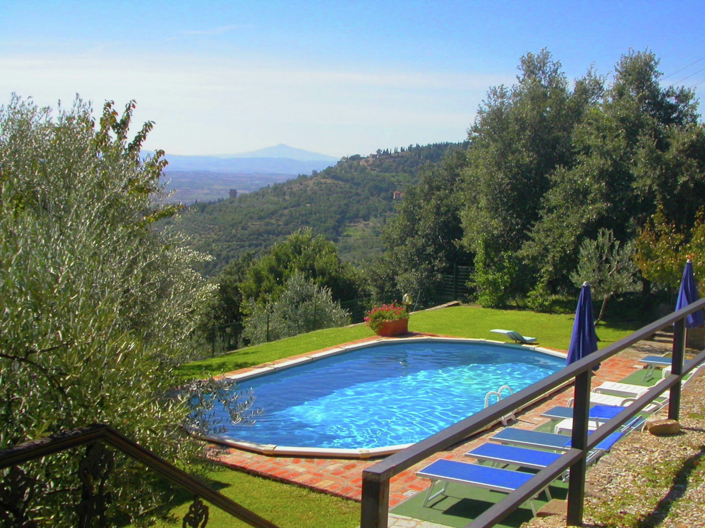 Piscina con vistas a un paisaje montañoso, rodeada de vegetación y un cielo despejado.
