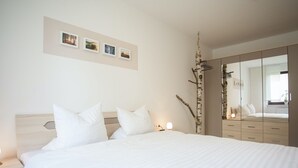 Quarto com cama grande, mesa de cabeceira, cômoda e espelho.