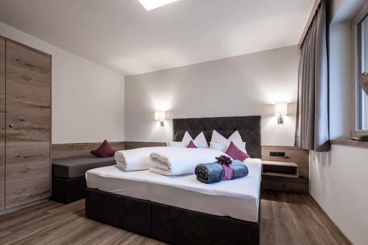 A modern bedroom with a large bed, bedside tables, and a wooden wardrobe.