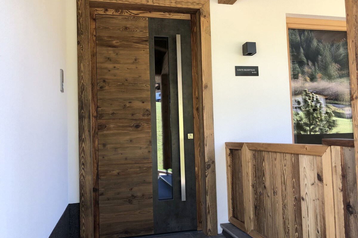 A wooden door with a glass panel, a sign reading "GASTE RECEPTION," and a framed landscape picture on the wall.