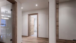 A modern hallway with wooden flooring, a glass door with a horse logo, and a view into a bathroom. - Farmhouse in Schwendau With Ski Storage (Schwendau)