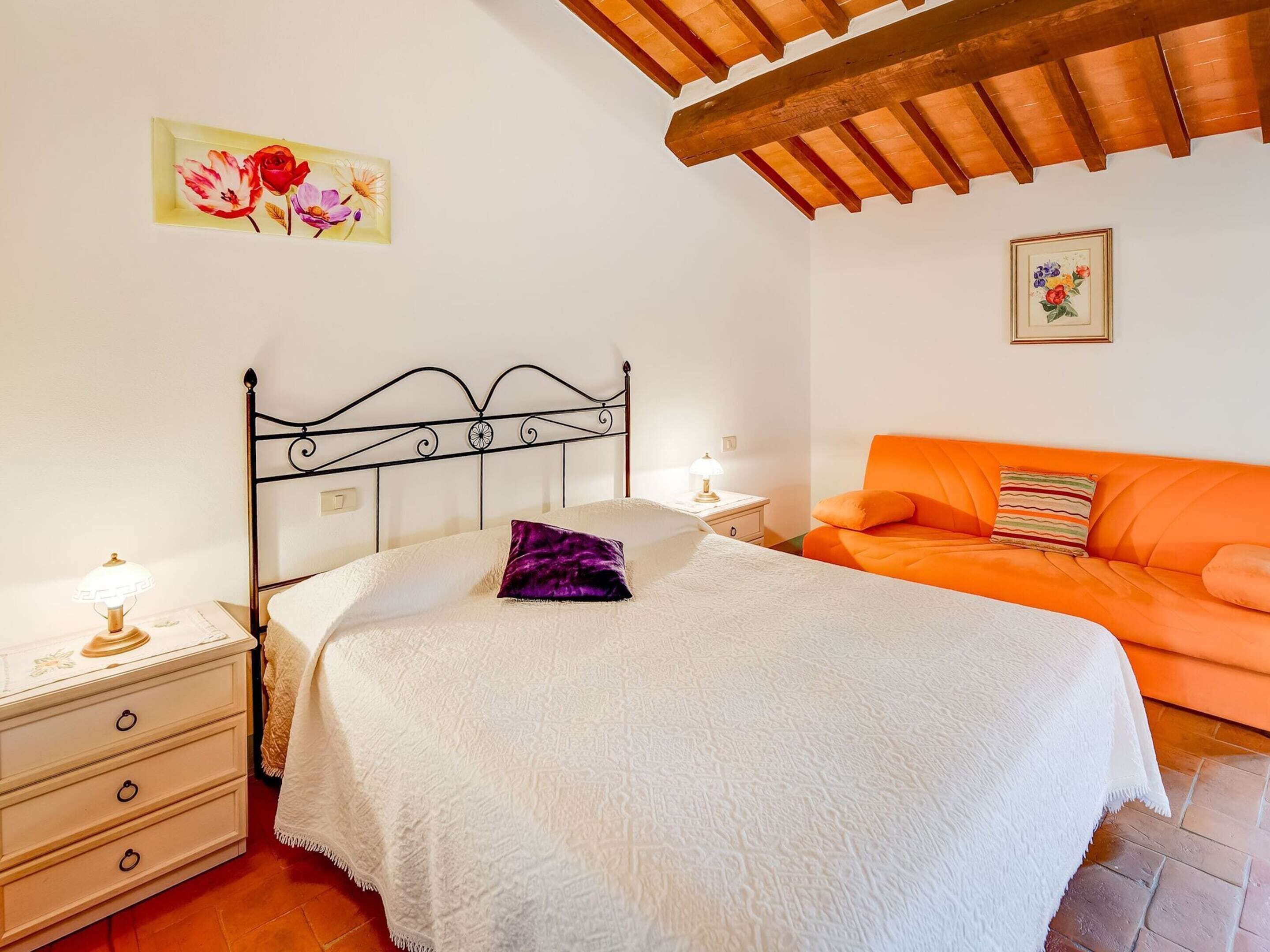 A bedroom with a bed, a nightstand, a dresser, an orange sofa, and a wooden ceiling.
