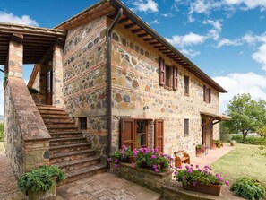 Un edificio de piedra con escalera de madera, un porche cubierto y macetas con flores.