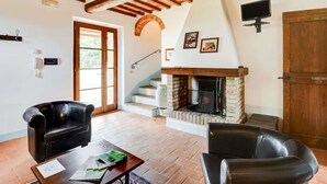 Un salon avec une cheminée, des fauteuils en cuir, un escalier en bois et une porte donnant sur l’extérieur.