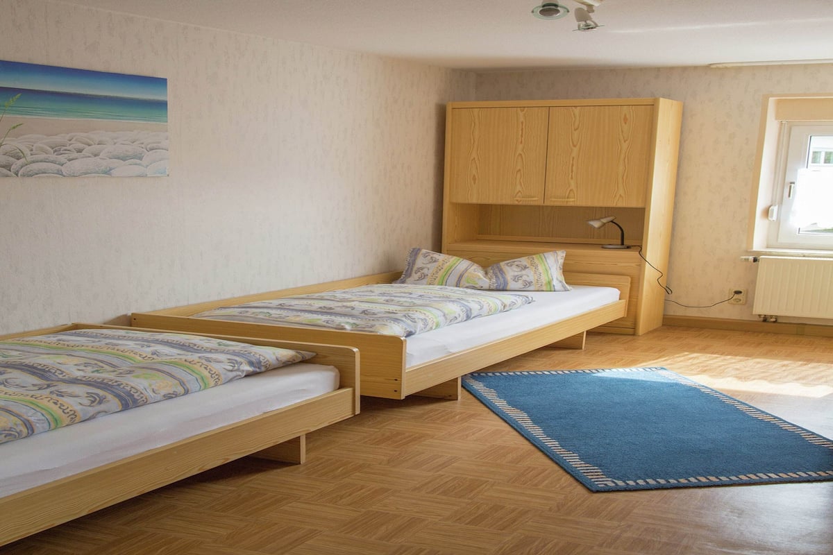 Une pièce avec deux lits en bois, un tapis bleu, une armoire en bois et une caméra fixée au plafond.