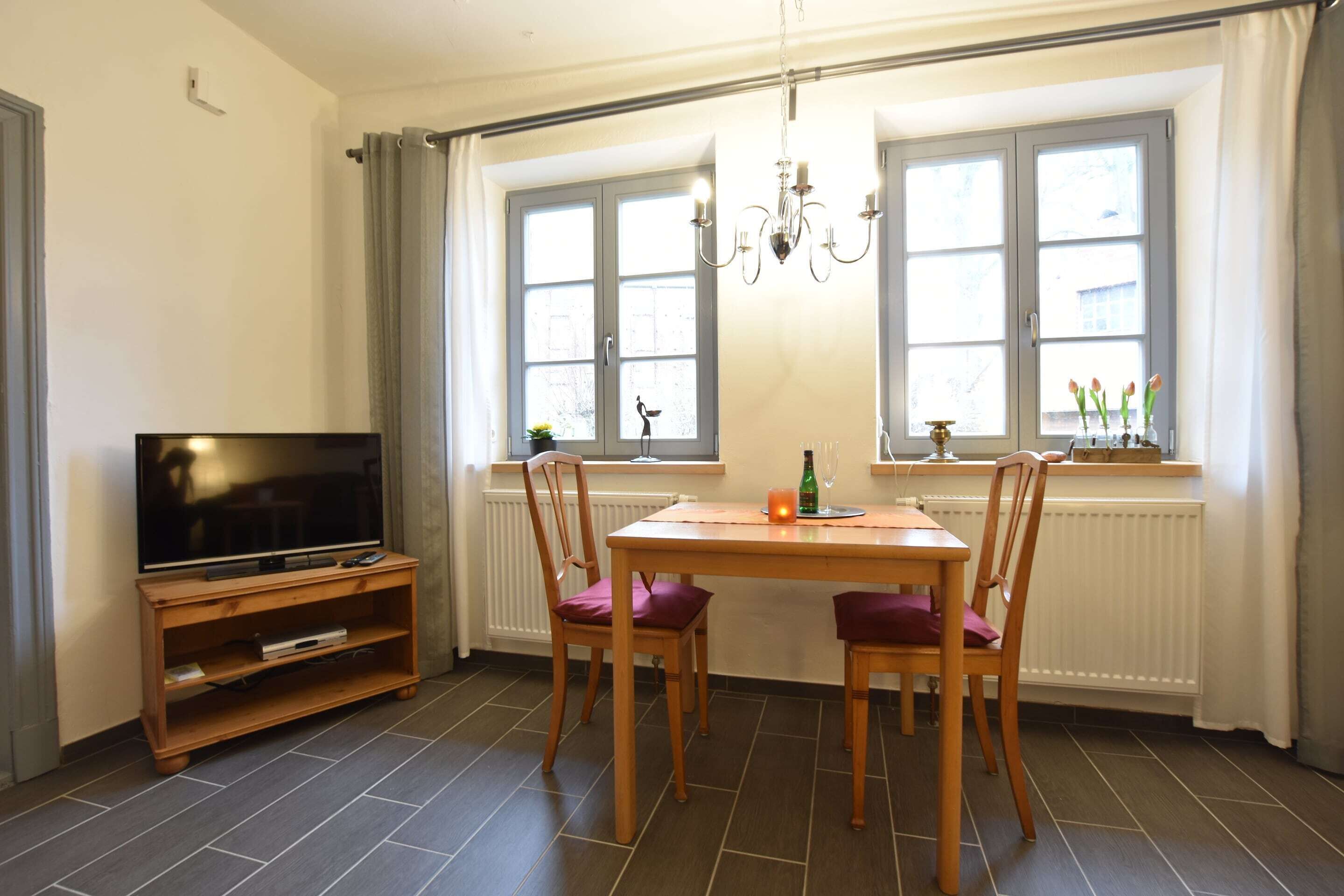 Een eethoek met een tafel, stoelen, een televisie op een standaard en een kroonluchter.