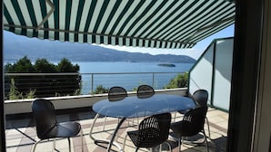 Une terrasse avec une table et des chaises, donnant sur un plan d’eau et des montagnes.