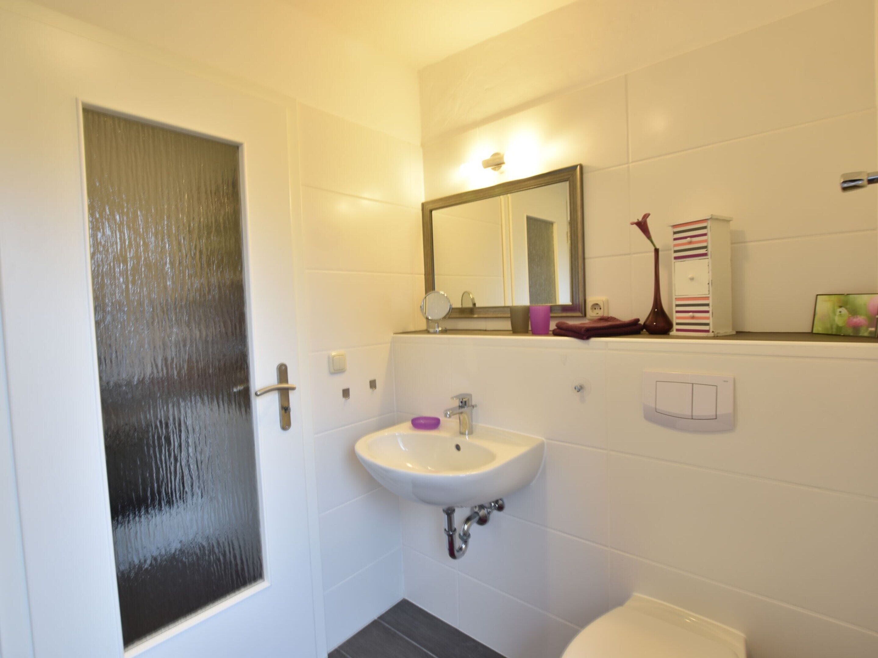Ein Badezimmer mit einem weißen Waschbecken, einem Spiegel, einer Toilette und einer Tür.