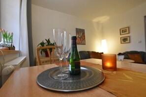 Une table à manger avec une bouteille et deux verres posés sur une assiette décorative, une bougie et une plante en arrière-plan.