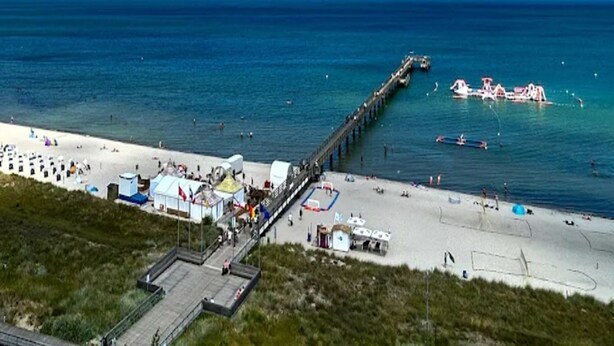Une plage avec une jetée qui s’avance dans la mer, une plage de sable et quelques bateaux.