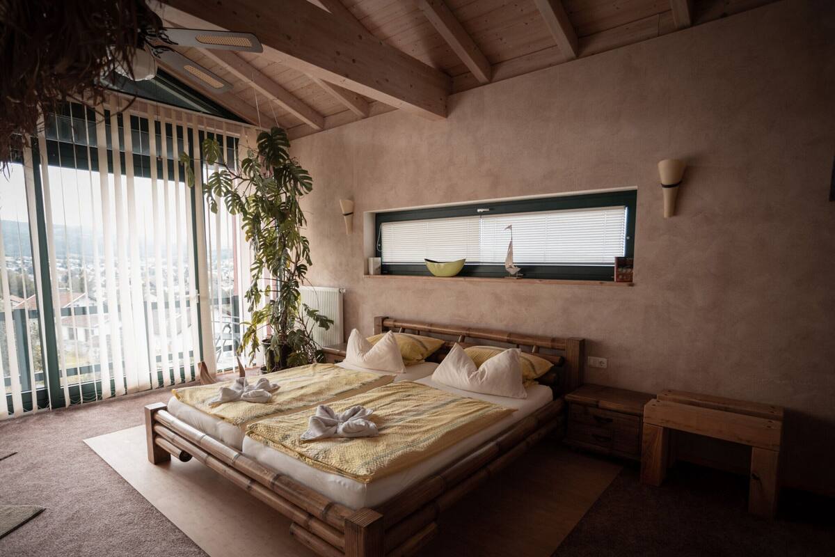 Ein modernes Schlafzimmer mit einem großen Bett, einem Holzkopfende und Blick auf die Stadt durch raumhohe Fenster.