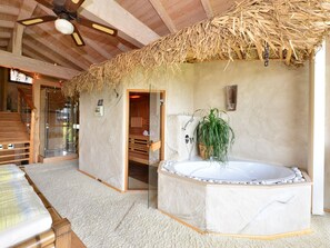 A spa room with a wooden ceiling, a glass-enclosed shower, a wooden bench, a massage table, and a large bathtub with a plant. - Tranquil Holiday Home in Blossersberg With Terrace (Viechtach)