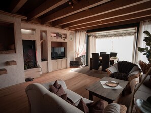 Ein gemütliches Wohnzimmer mit Fernseher, bequemen Sitzgelegenheiten und einem Essbereich mit Tisch und Stühlen.