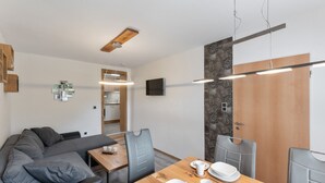 A modern dining area with a wooden table set for two, grey upholstered chairs, and a kitchen in the background. - Pretty Apartment in Medebach With Adjacent Forest (Medebach)