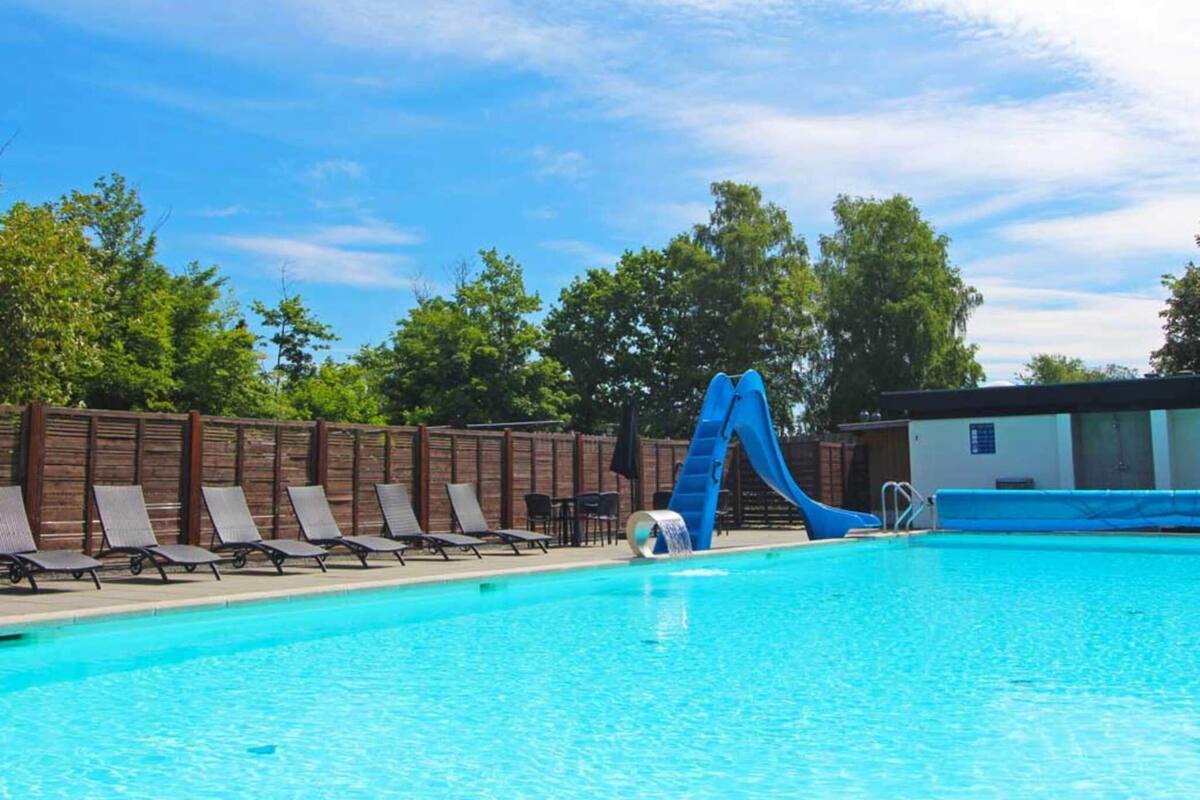 Ein Swimmingpool mit blauer Rutsche, Liegestühlen und einem Holzzaun.