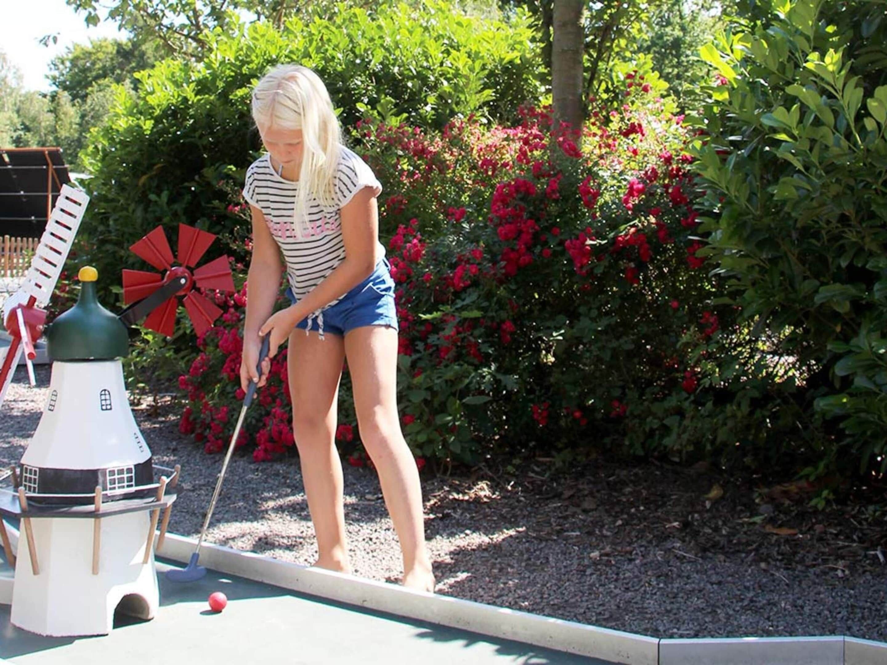 A person playing miniature golf in a garden with a windmill and a lighthouse model.