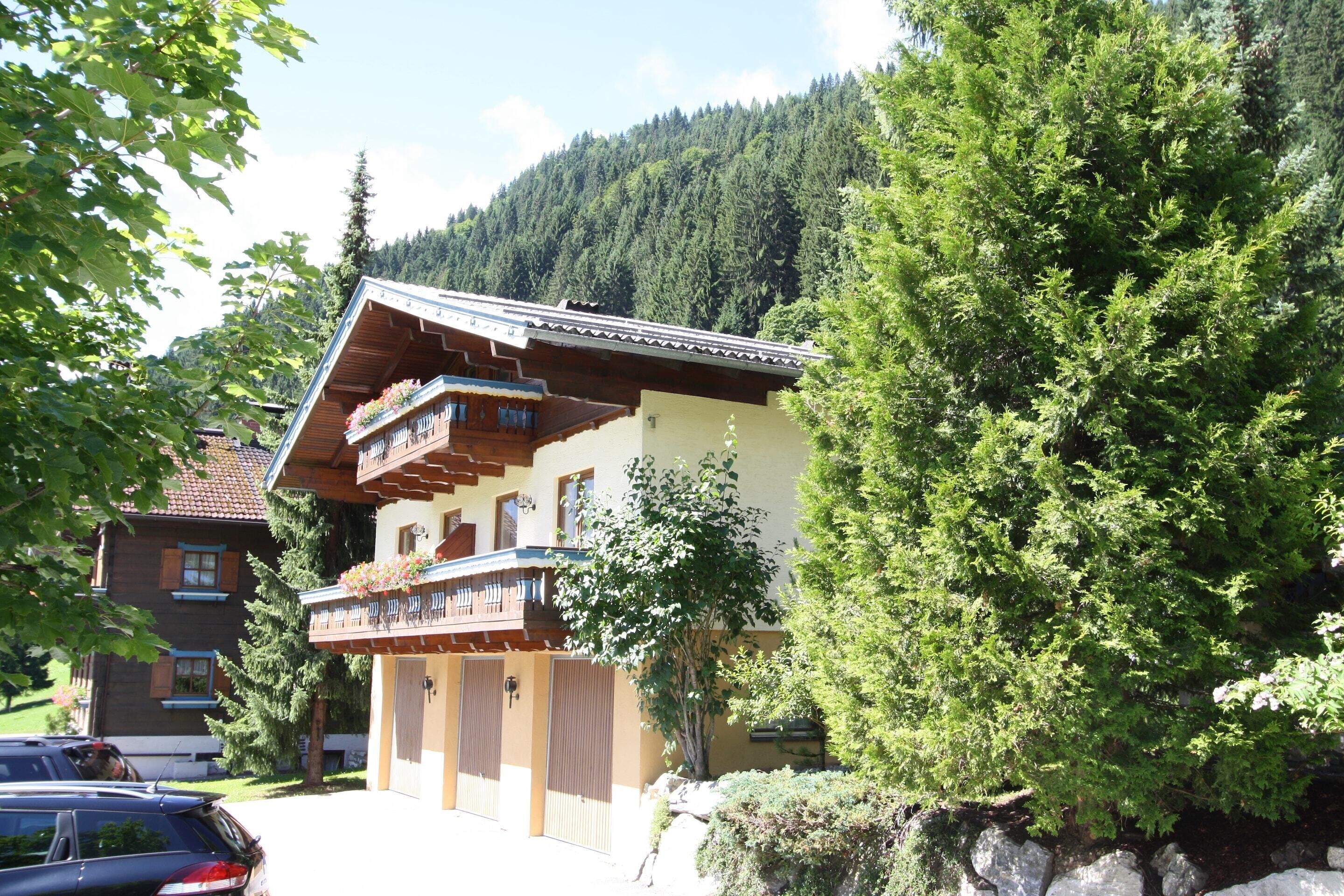 Ein traditionelles Chalet mit Holzbalkon, umgeben von üppiger Vegetation und einem Bergpanorama.