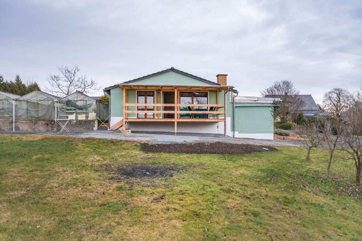 A single-story house with a porch, a green roof, and a small garden area in front.