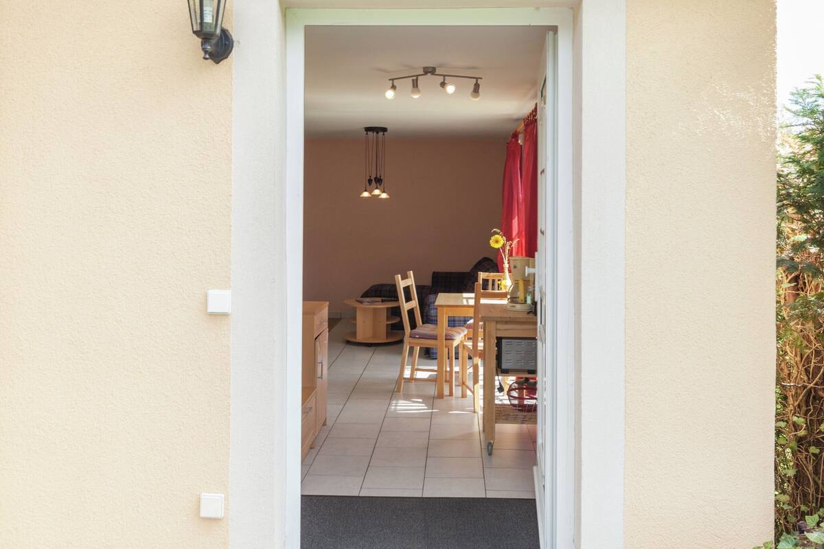 A doorway leading to a dining area with a table and chairs, a hanging light fixture, and a red curtain.