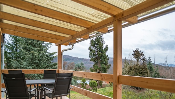 A covered outdoor deck with a table and chairs, overlooking a natural landscape with trees and hills. - Modern Holiday Home With Shared Swimming Pool in Mittelndorf (Sebnitz)
