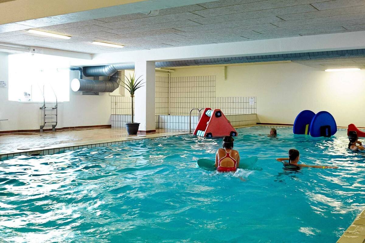 Una piscina interna con una scala, una struttura gioco rossa e blu e una pianta in vaso.