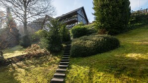 Un escalier en pierre mène à un bâtiment moderne doté de balcons, le tout étant entouré d’une végétation luxuriante et d’arbres.
