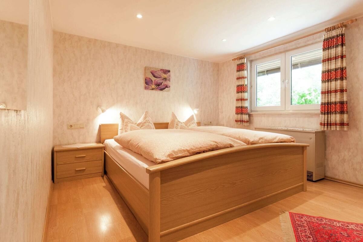 Une chambre à coucher avec un lit en bois, des lampes de chevet, une fenêtre avec des rideaux et un tapis rouge.