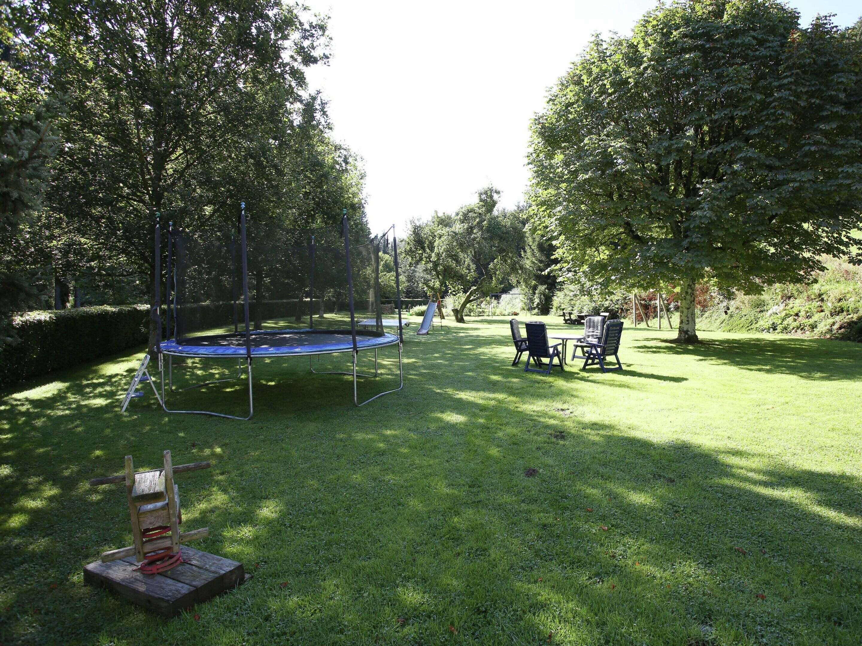 Een gazon met een trampoline, een picknicktafel en twee stoelen.