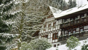 Un chalet traditionnel doté d’un toit à forte pente, de balcons en bois et entouré d’un paysage enneigé.