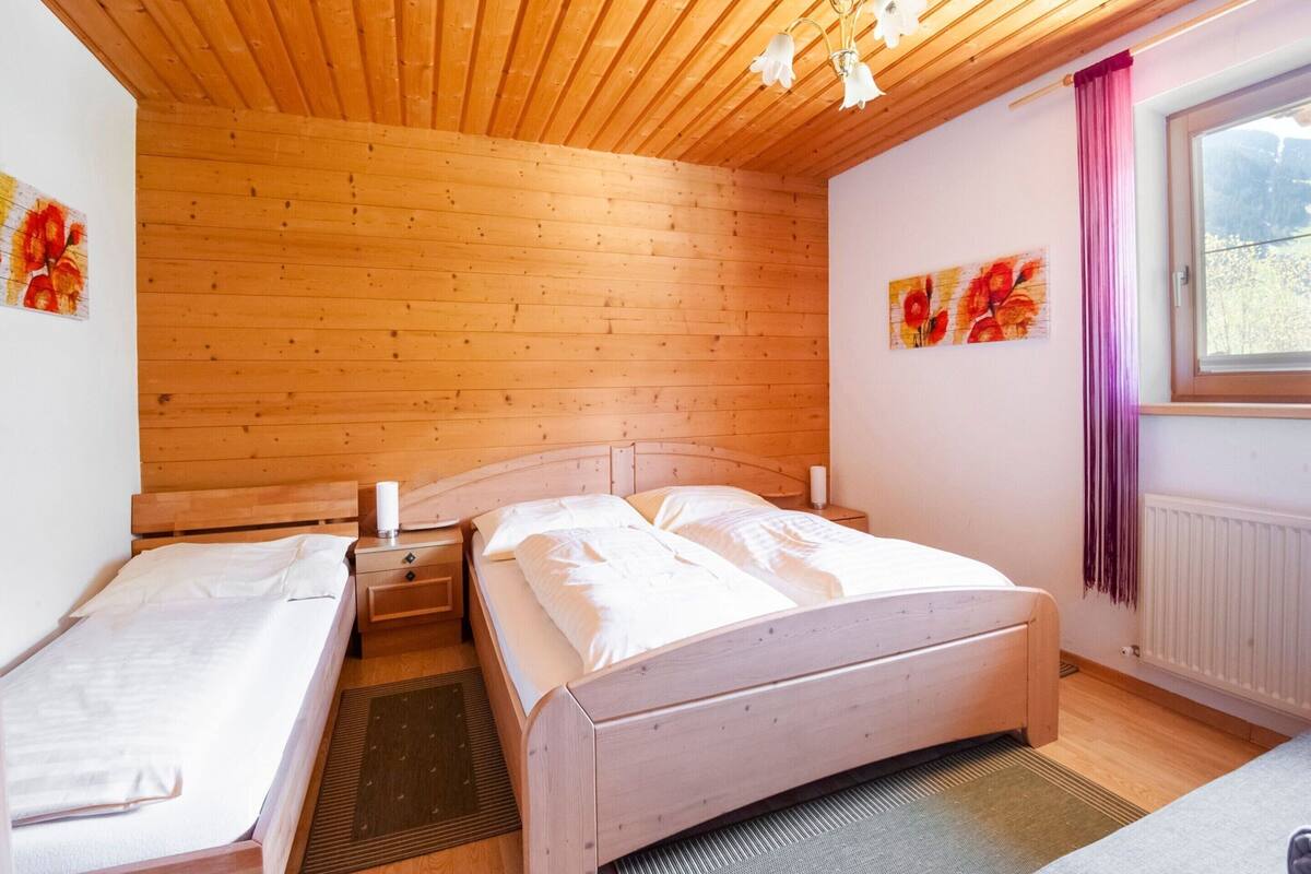 A bedroom with a wooden ceiling, two single beds, a large bed, a window with a view, and artwork on the walls.