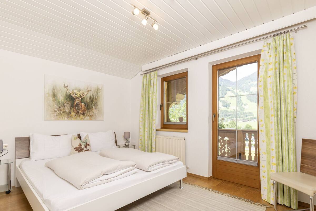 A bedroom with a double bed, a window with curtains, a radiator, and a painting on the wall.
