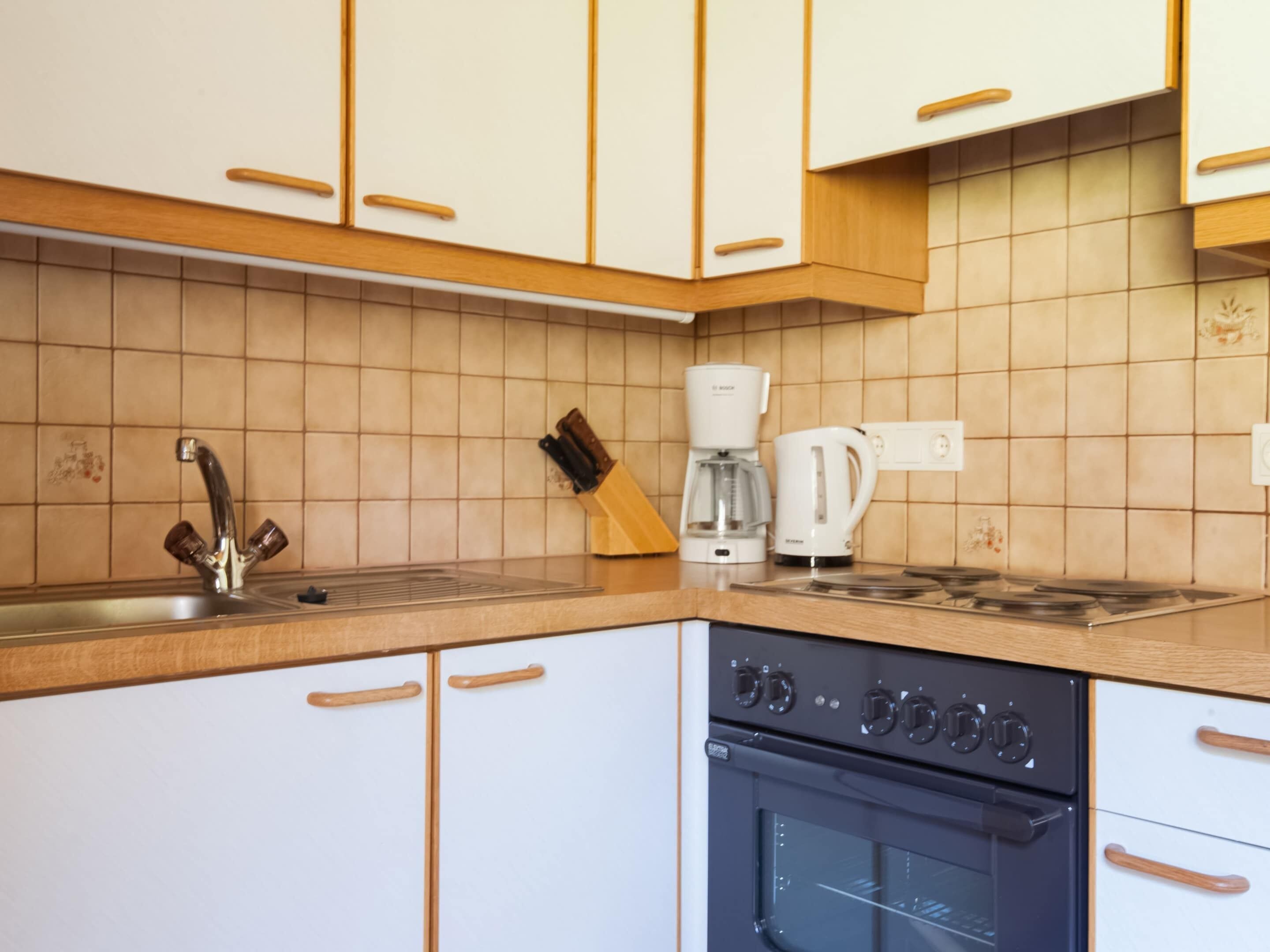 A kitchen with white cabinets, a stainless steel sink, a Bosch coffee maker, and a black oven.