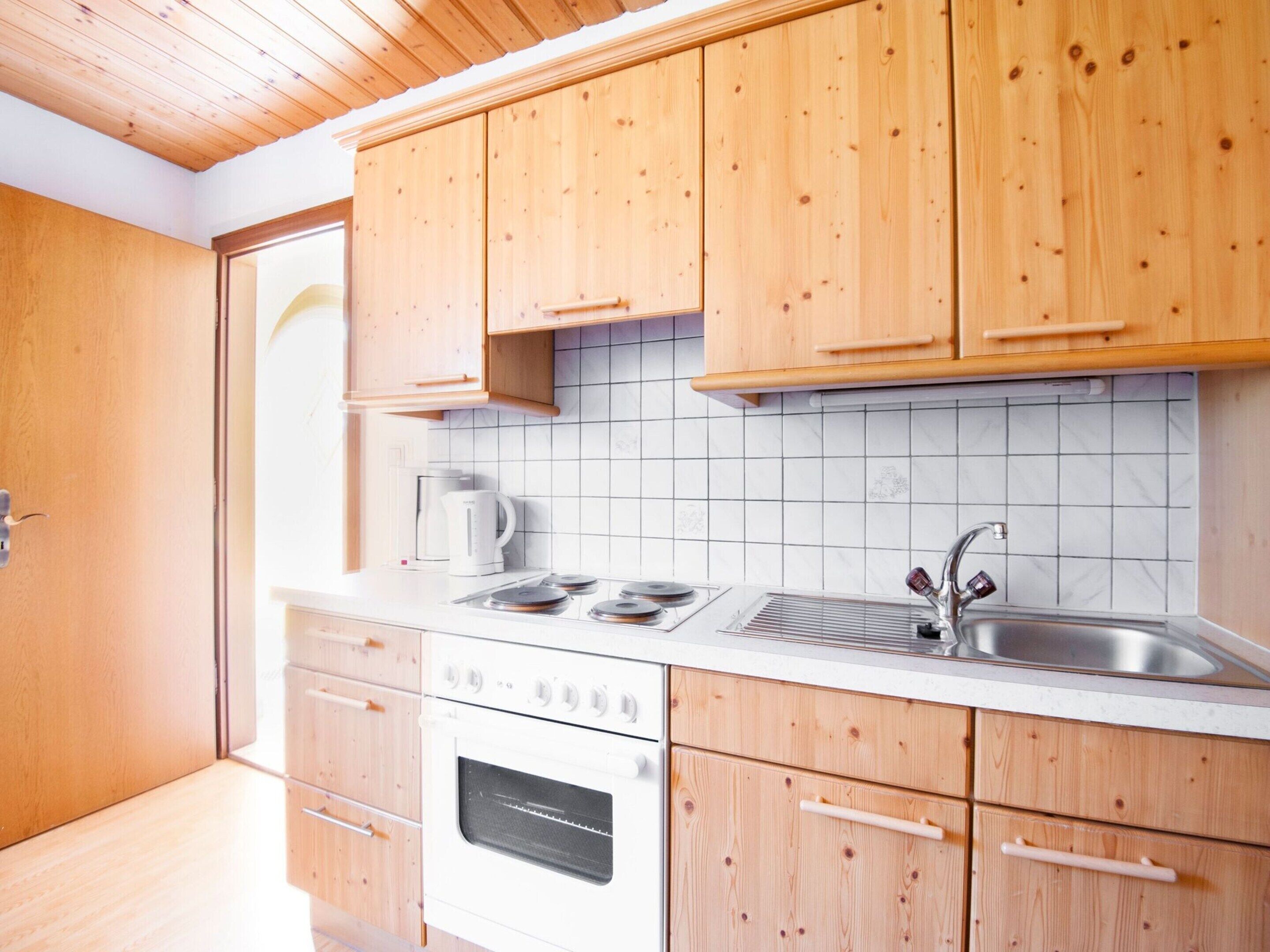 A kitchen with wooden cabinets, a white countertop, a stove, an oven, a sink, and a coffee maker.