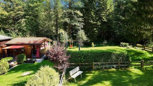 A wooden cabin with a red roof, surrounded by lush greenery and a wooden fence.