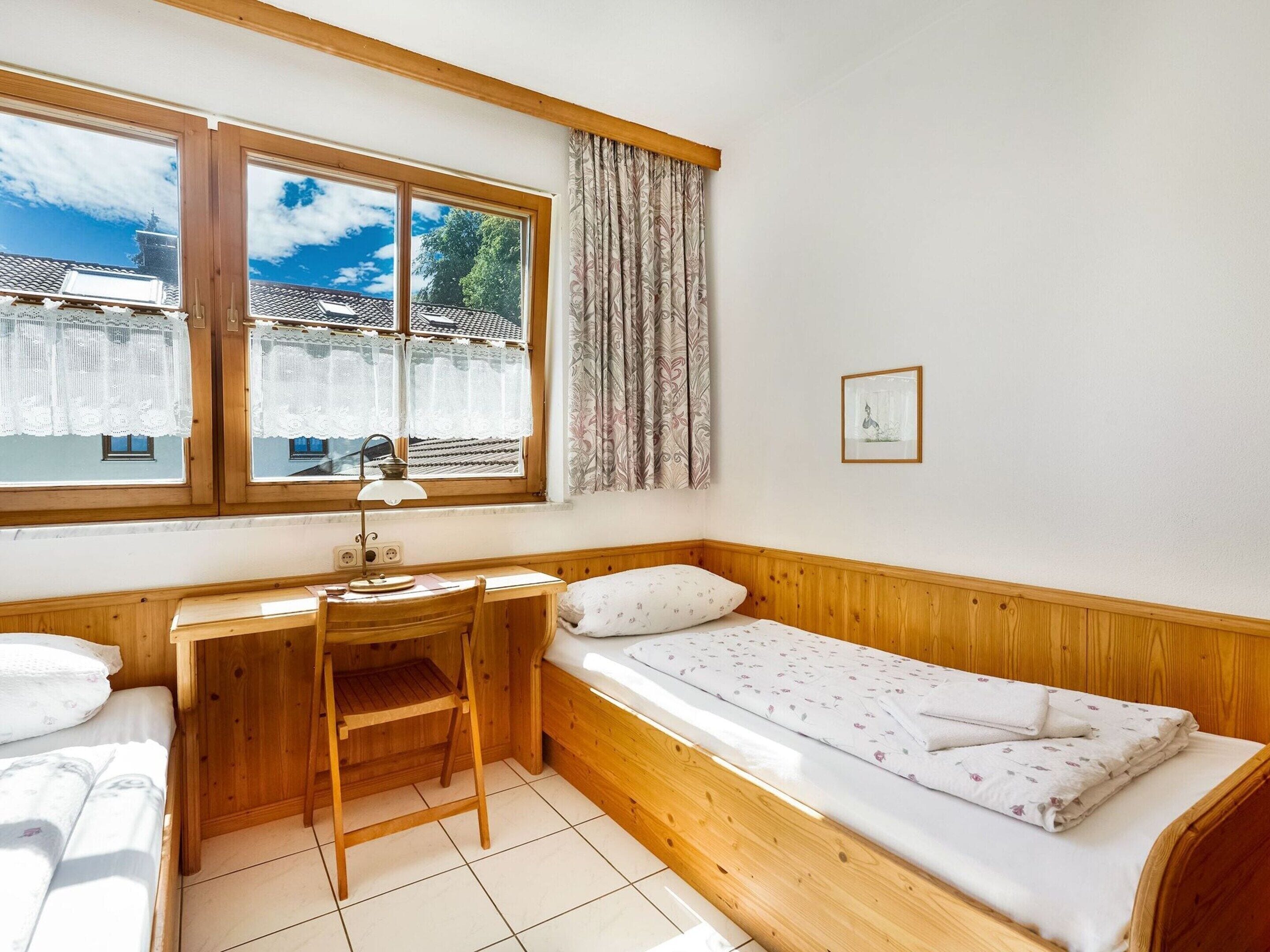 Ein kleines, gemütliches Zimmer mit einem Holztisch, einem Einzelbett und einem Fenster mit Vorhängen.