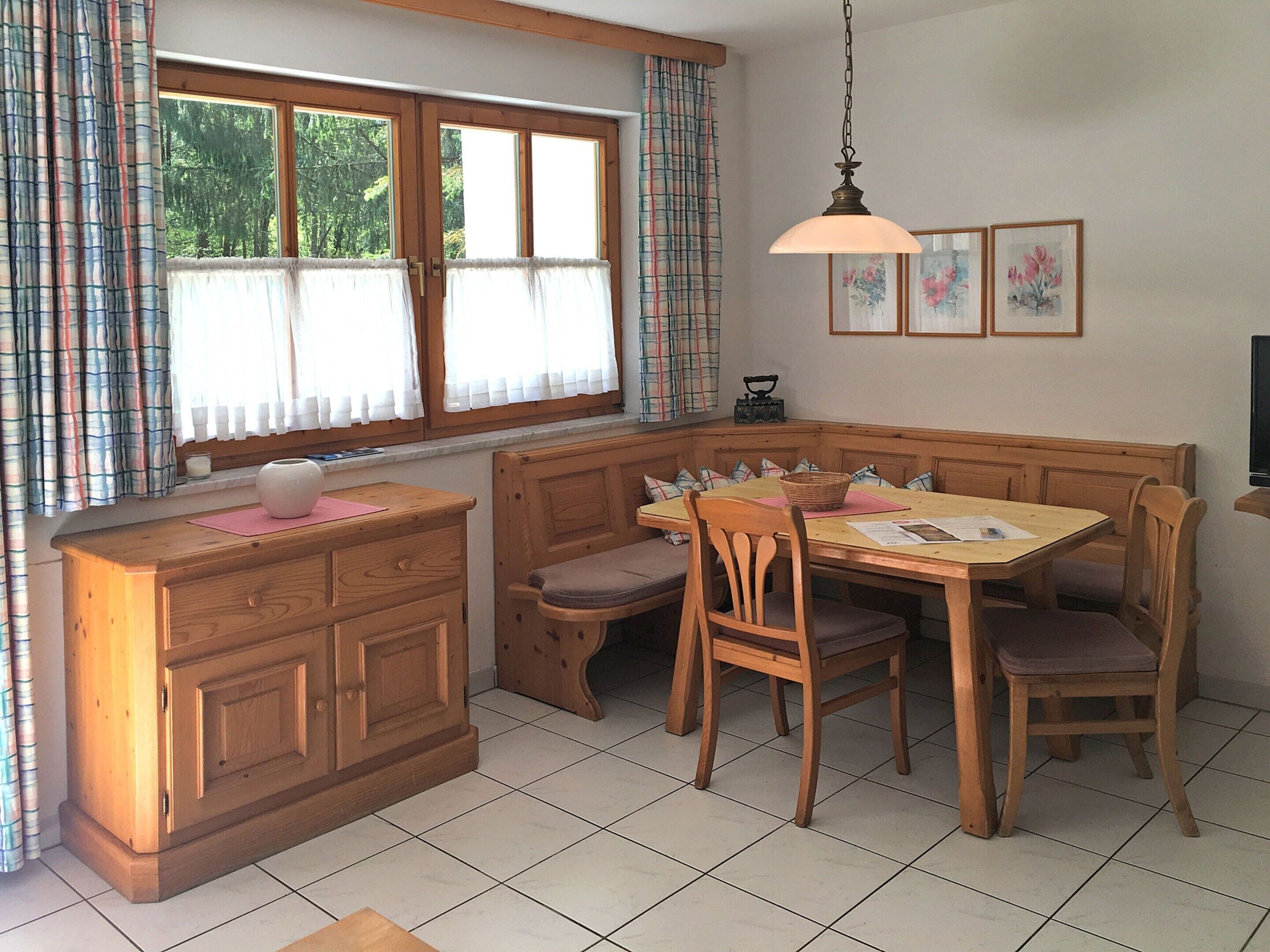 Una cocina acogedora con una mesa de madera y un banco, un armario y una ventana con cortinas.