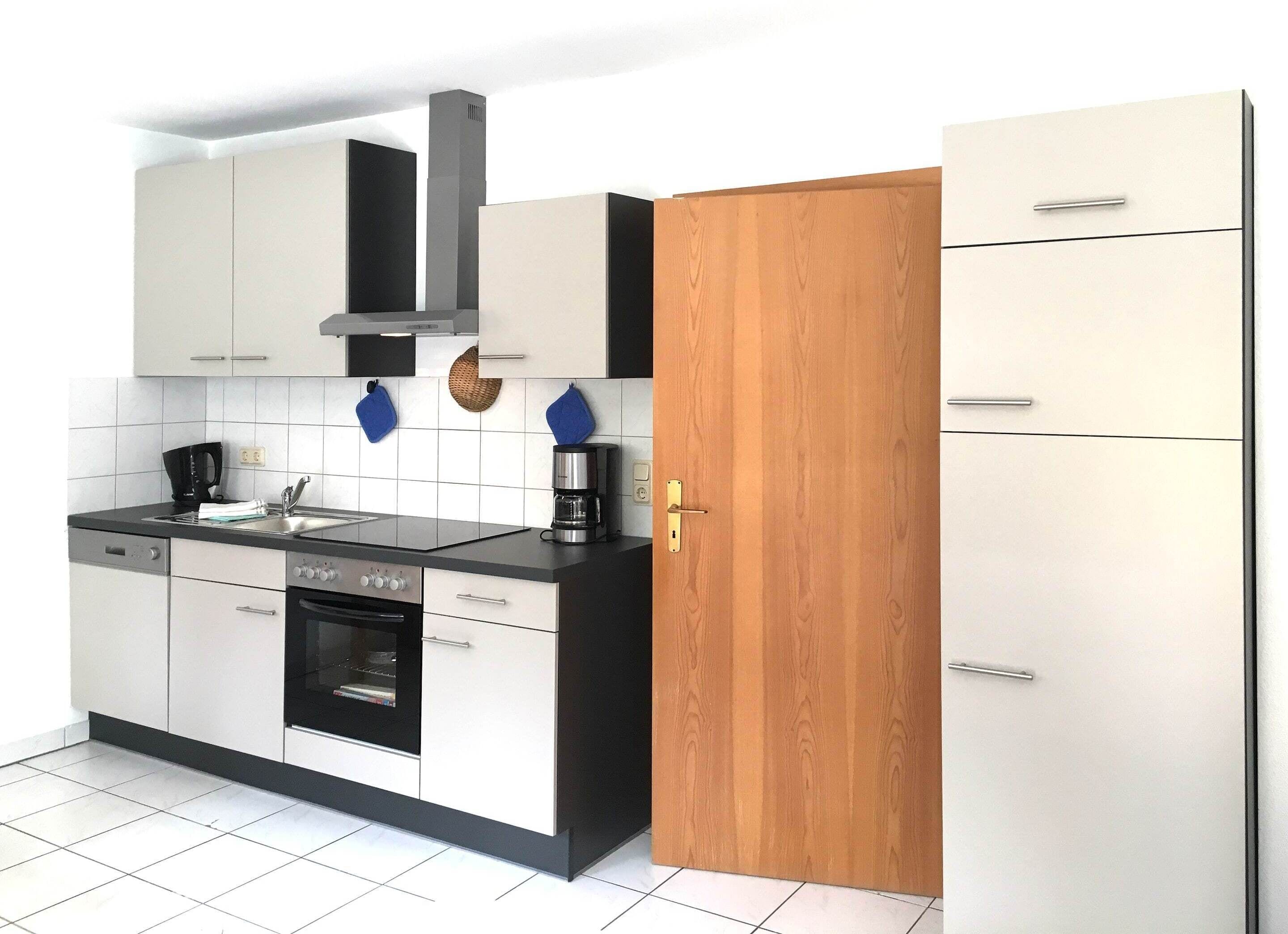Una cocina moderna con armarios blancos, encimera negra, horno integrado y cafetera.