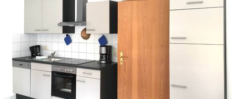 Una cocina moderna con armarios blancos, encimera negra, horno integrado y cafetera.