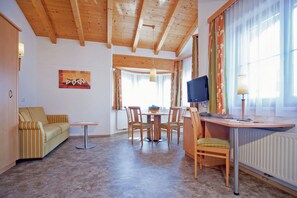 Een kamer met een houten plafond, een bank, een eettafel met stoelen, een televisie en een lamp.