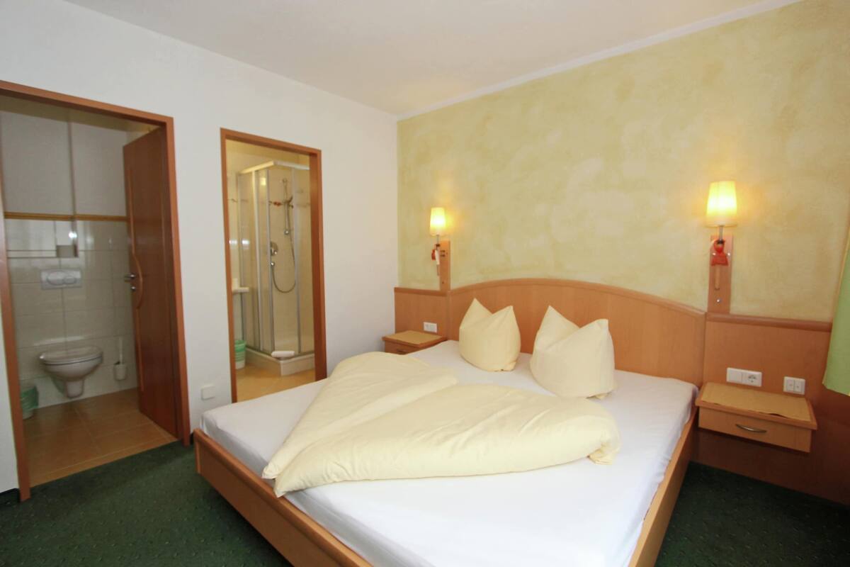 Una camera d'albergo con un letto, comodini, uno specchio, una doccia e un bagno.