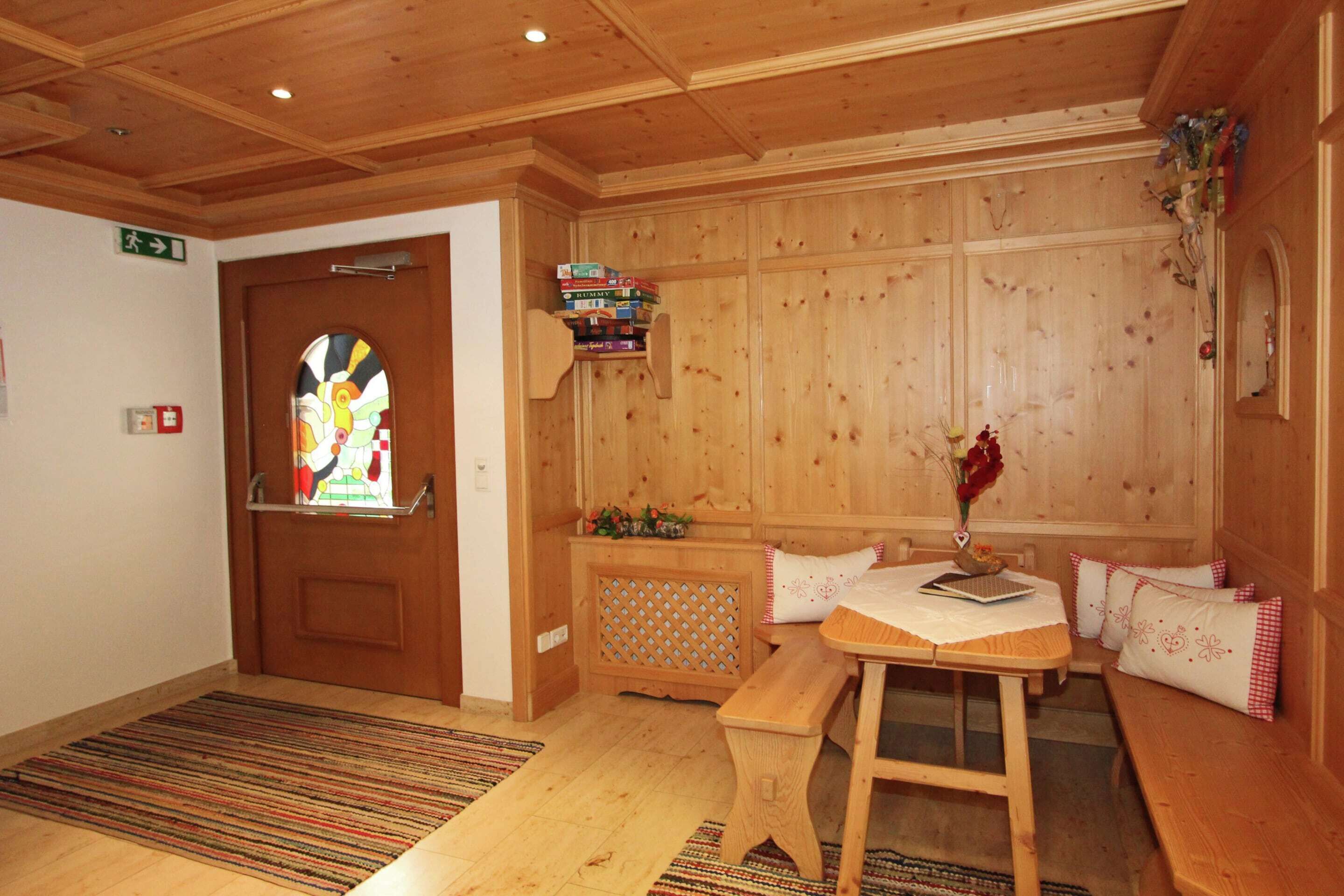 Un interno in legno con una panca, un tavolo, uno scaffale pieno di libri e una porta con una finestra a vetri colorati.