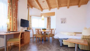 Une pièce chaleureuse avec un plafond en bois, une table à manger avec des chaises, un lit avec un coussin à rayures et un téléviseur posé sur un bureau.