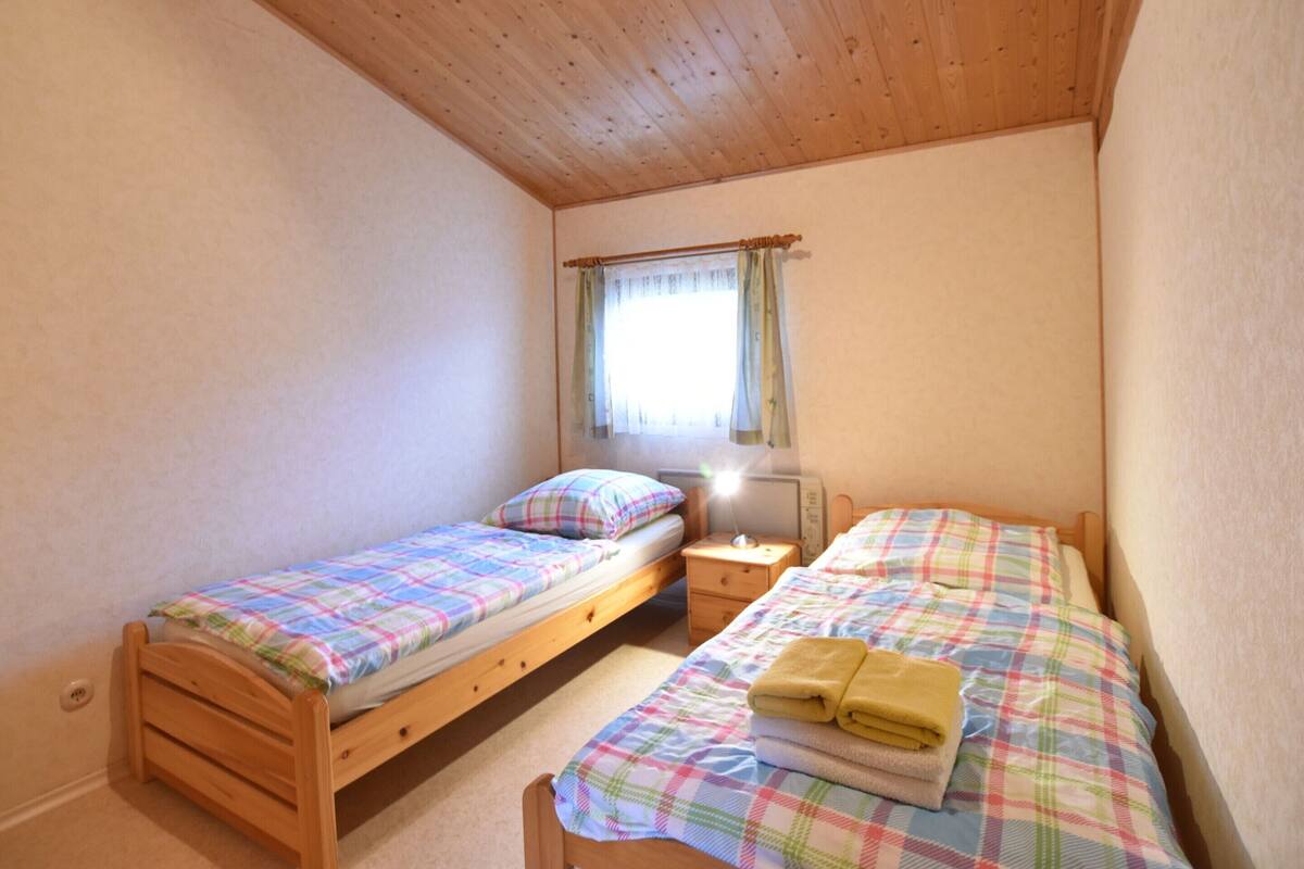 Une petite chambre confortable avec deux lits simples, une table de chevet, une lampe et une fenêtre avec des rideaux.