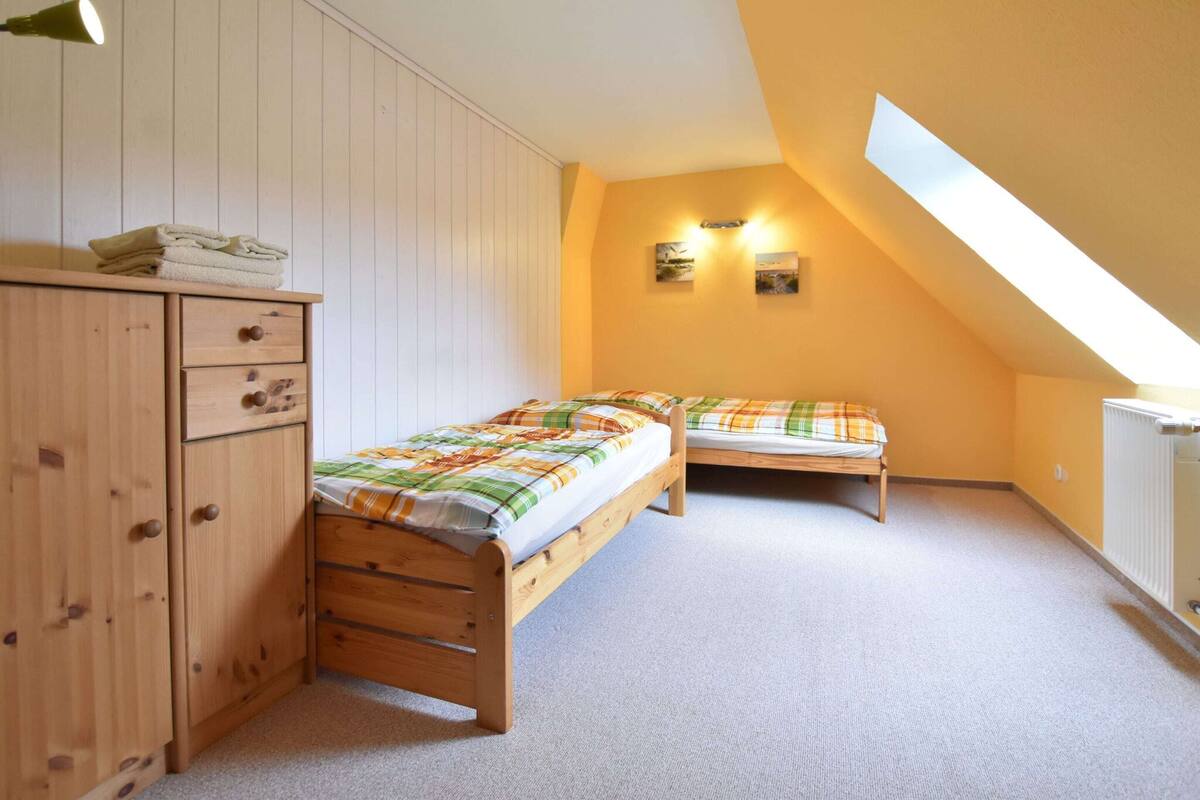 Une petite chambre mansardée, chaleureuse et accueillante, avec deux lits en bois, une armoire en bois et un puits de lumière.