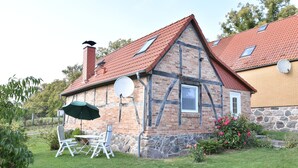 Perinteinen, osittain puurunkoon rakennettu talo, jossa on punatiilestä tehty katto, satelliittiantenni ja pieni puutarha, jossa on pöytä ja tuoleja.