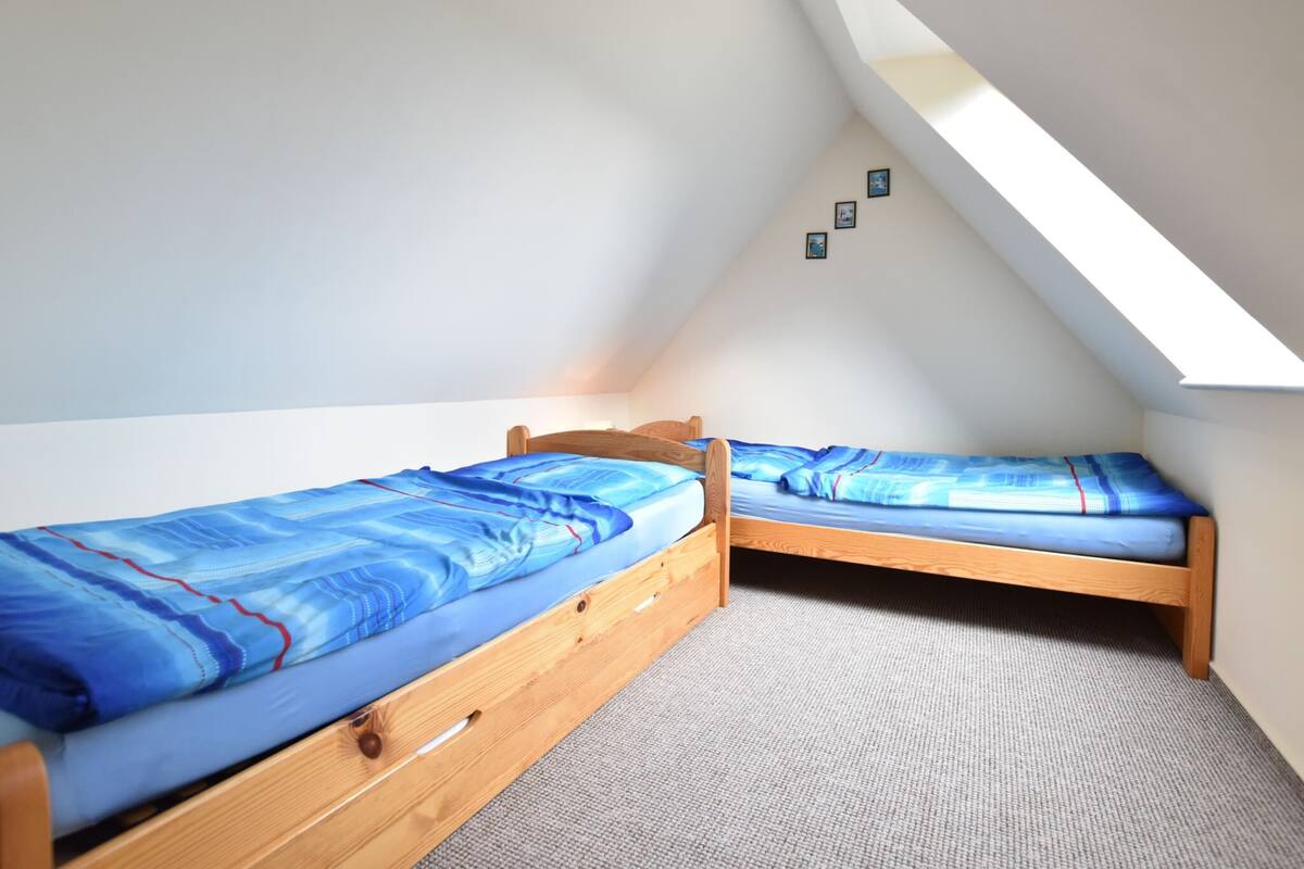 Une petite pièce aux murs inclinés, avec deux lits en bois, un sol recouvert de moquette et une lucarne.