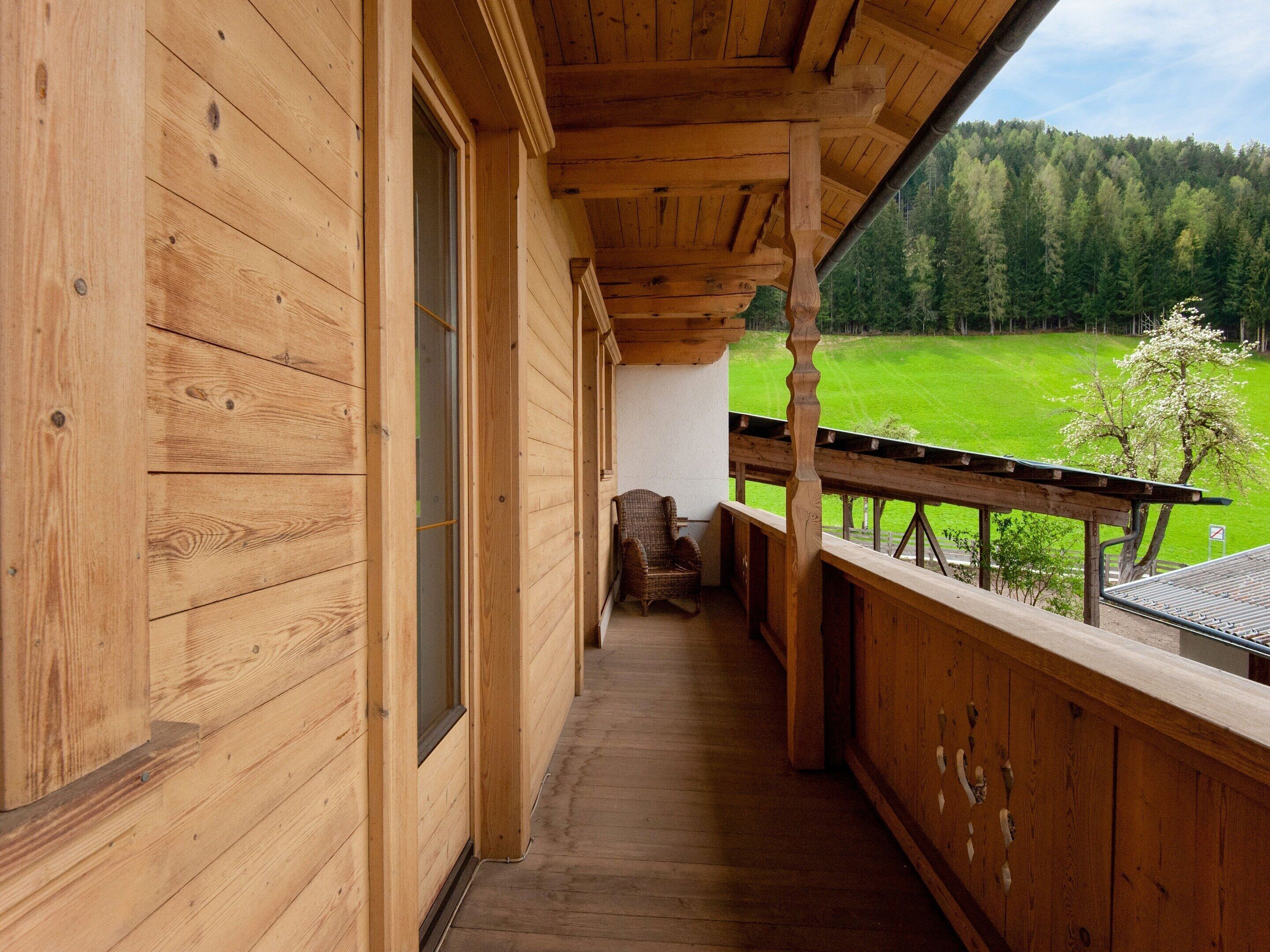 Un balcón de madera con vistas a un campo verde y árboles.