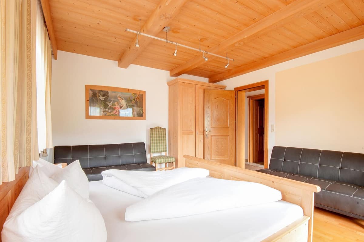 A room with a bed, a sofa, a wooden wardrobe, and a painting on the wall.