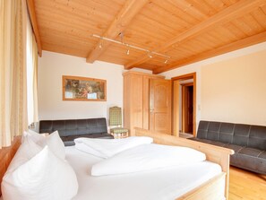 A room with a bed, two sofas, a wooden wardrobe, and a painting on the wall.